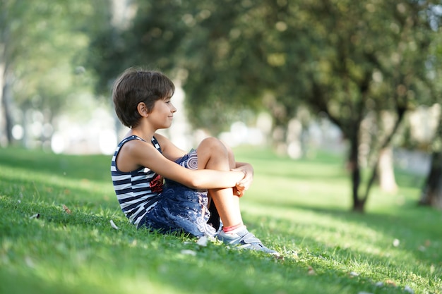 Little girl, eight years old, sitting on the grass outdoors.