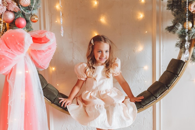 Photo a little girl in an elegant dress is sitting on a hanging swing decorated with christmas decorations