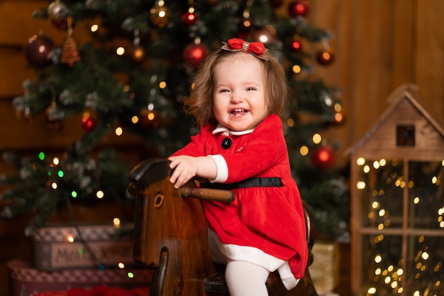 Little girl in a festive red dress on a wooden swing rocking horse.