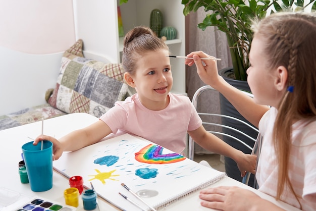 Little girl getting her face painted by older sister at the table