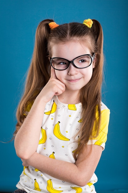 Little girl in glasses and banana T-Shirt on blue background