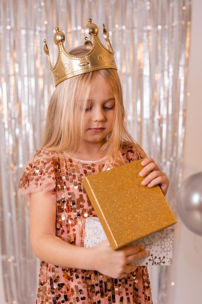 A little girl in a gold crown holds a gift box with the word birthday on it.