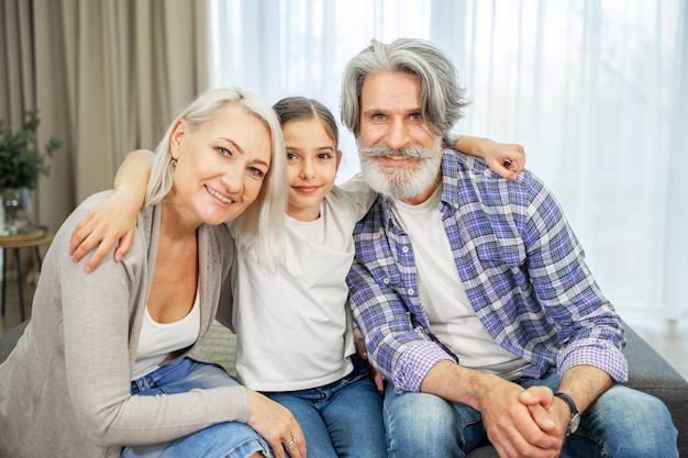 little girl granddaughter and her retired  grandparents sitting on sofa in living room 