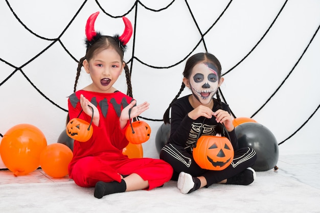 Little girl in halloween carnival costume with Jack o lantern (pumpkin) and balloon. Asian cute children tease each other cheerfully.