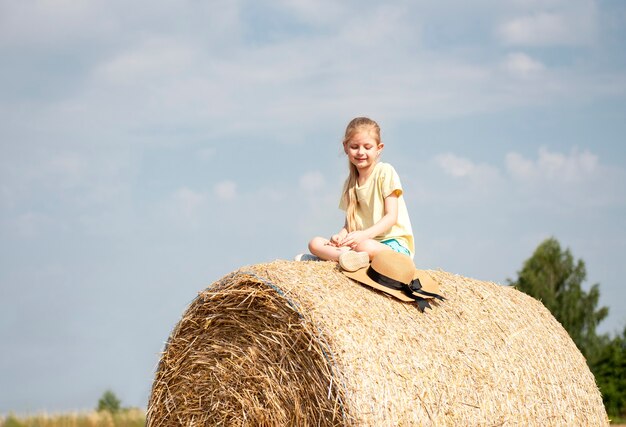 Little girl having fun in a wheat field on a summer day. Child playing at hay bale field during harvest time.