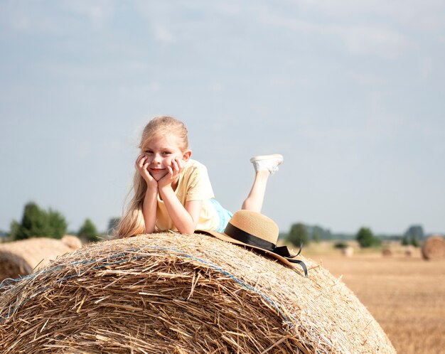 Little girl having fun in a wheat field on a summer day. Child playing at hay bale field during harvest time.