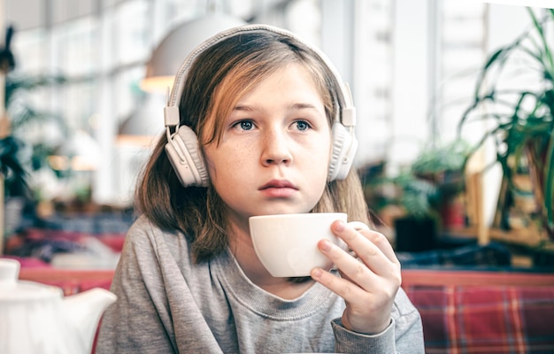 A little girl in headphones in a cafe with a cup of tea