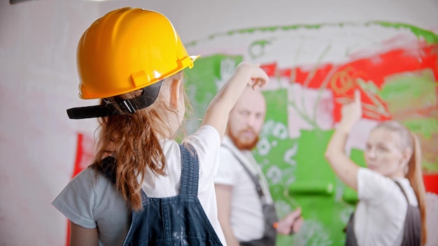 A little girl in a helmet pointing at the wall  her parents standing next to the wall