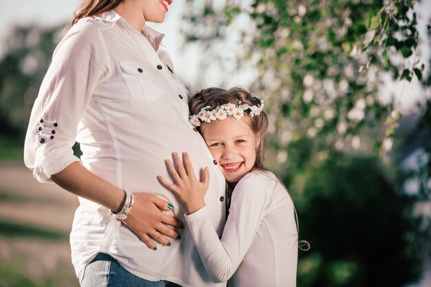 Photo little girl and her happy pregnant mom on a walk in the summer park