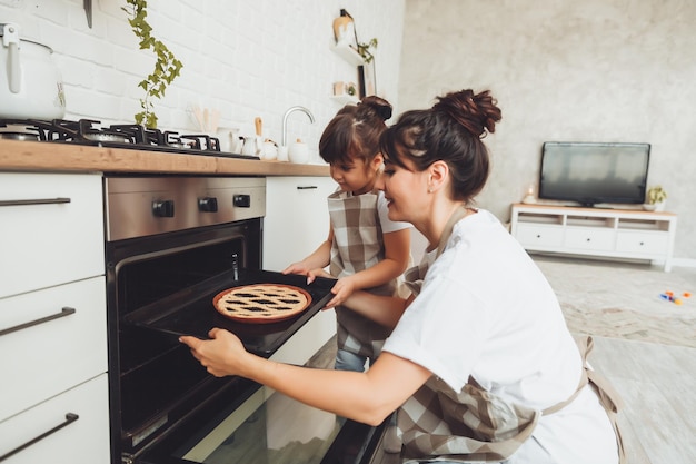 A little girl and her mom put a baking dish with a pie in the oven in the kitchen mom and child cook a pie together in the kitchen