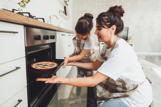 A little girl and her mom put a baking dish with a pie in the oven in the kitchen mom and child cook a pie together in the kitchen