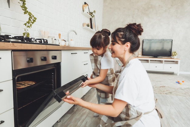 A little girl and her mom put a baking dish with a pie in the oven in the kitchen mom and child cook a pie together in the kitchen