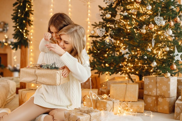 Little girl and her mom sitting near Christmas tree and hugging