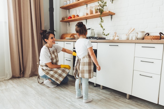 A little girl and her mother are cleaning the kitchen a woman and a child wipe the oven in the kitchen house cleaning helping mom