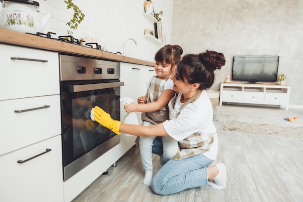 A little girl and her mother are cleaning the kitchen a woman and a child wipe the oven in the kitchen house cleaning helping mom