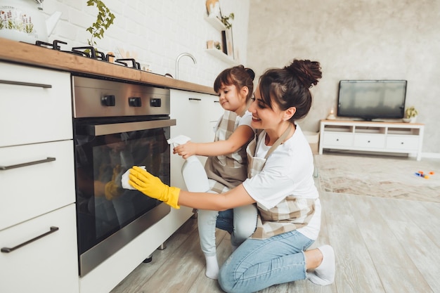 A little girl and her mother are cleaning the kitchen a woman and a child wipe the oven in the kitchen house cleaning helping mom