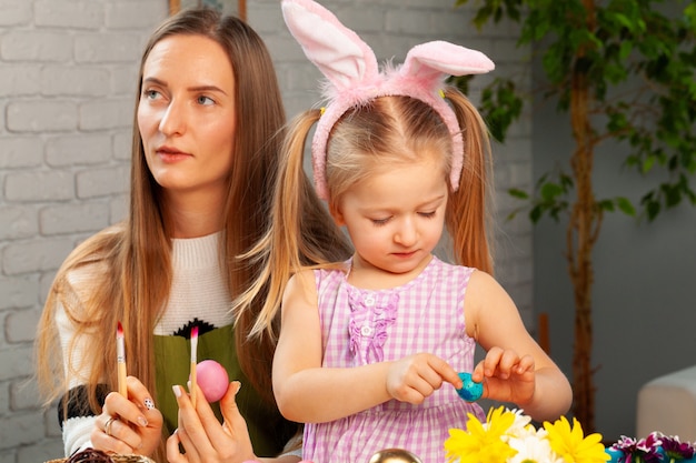 Little girl and her mother coloring eggs for Easter together