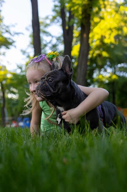 A little girl hid behind a french bulldog she hugged him and together they look good to the side