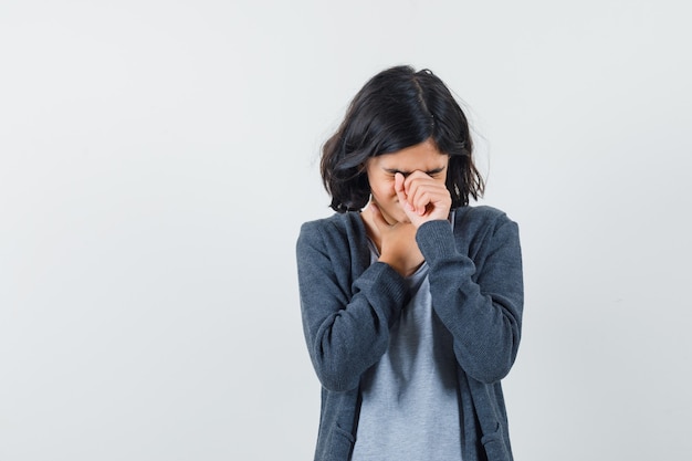 Little girl holding hand on face in t-shirt, jacket and looking depressed. front view.