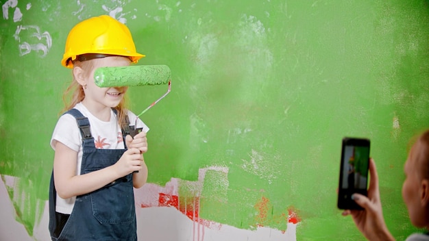 A little girl holding a paint roller  her parent takes a photo of their daughter