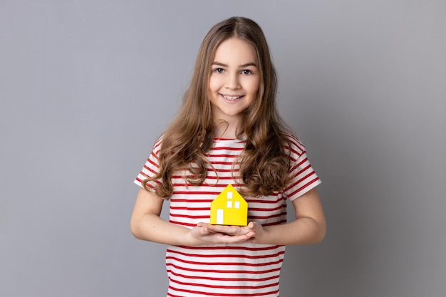 Little girl holding paper house smiling to camera advertisement of trustworthy real estate agency