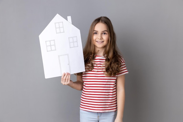 Little girl holding paper house and smiling friendly advertising realtor services house purchase