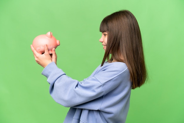 Little girl holding a piggybank over isolated chroma key background with happy expression