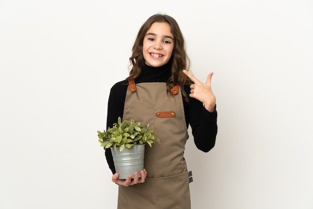 Little girl holding a plant isolated on white background giving a thumbs up gesture