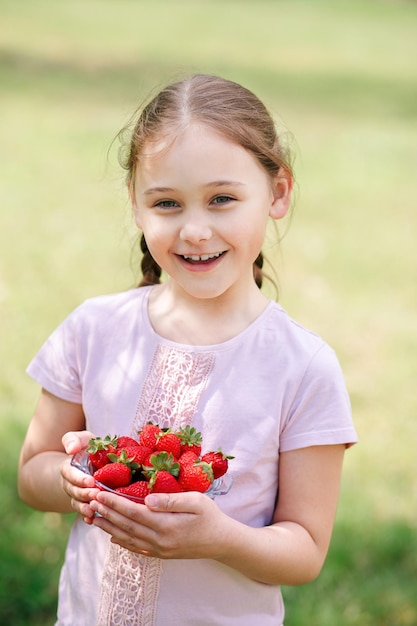 Little Girl Holding plate with Strawberries in nature Gardening and agriculture concept Vegan vegetarian Vertical