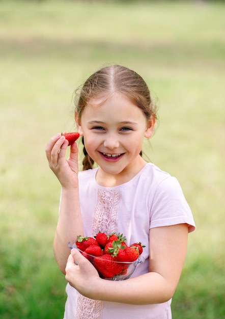 Little Girl Holding plate with Strawberries in nature Gardening and agriculture concept Vegan vegetarian Vertical