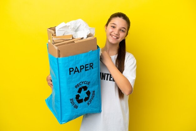 Little girl holding a recycling bag full of paper to recycle over isolated yellow background celebrating a victory