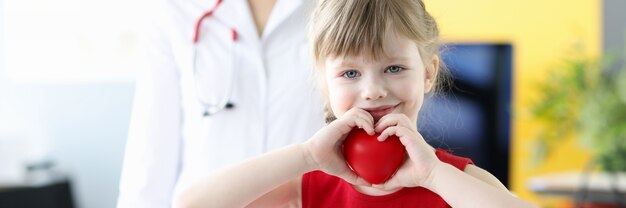 Little girl holding red toy heart in her hands in doctors office childrens health concept