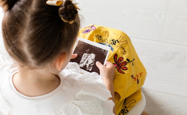 Little girl holding ultrasound image of the fetus on her hands. Parenting concept.