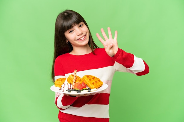 Little girl holding waffles over isolated chroma key background happy and counting four with fingers