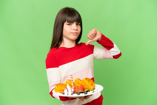 Little girl holding waffles over isolated chroma key background proud and selfsatisfied