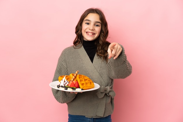 Little girl holding waffles isolated surprised and pointing front