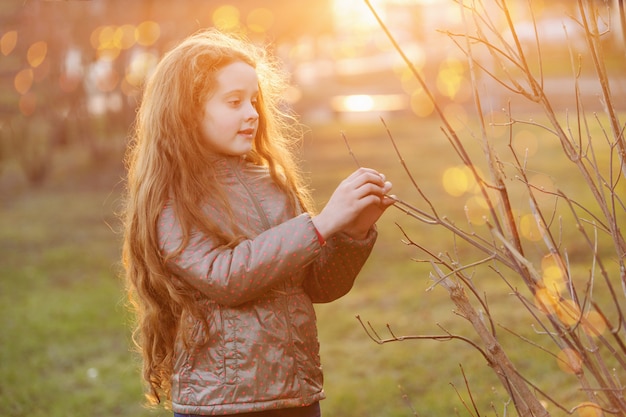 Little girl holding young green tree branch in sunlight.