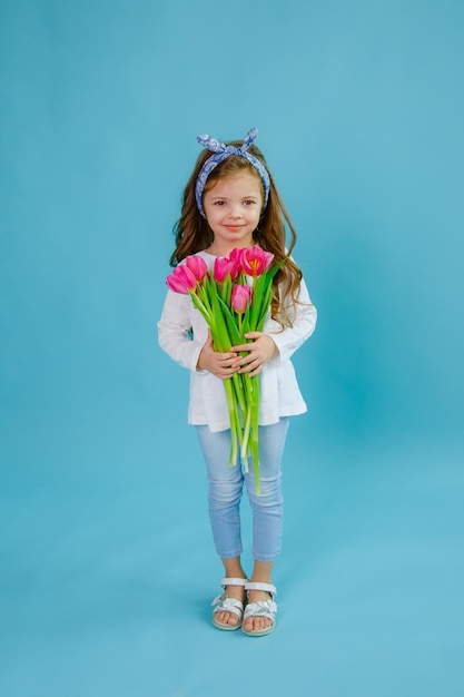 A little girl holds a bouquet of pink tulips on a blue background