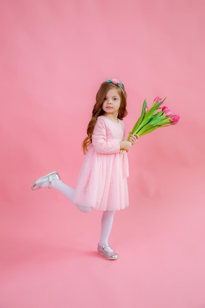 A little girl holds a bouquet of pink tulips on a pink background