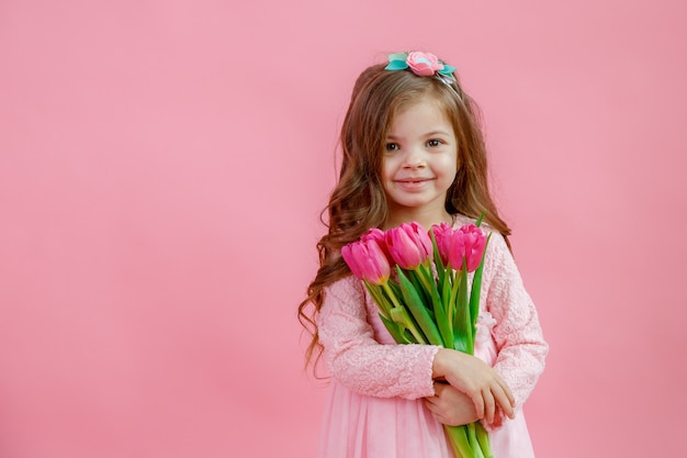 Little girl holds a bouquet of tulips on a pink background