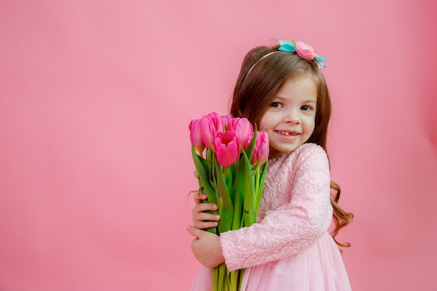 Little girl holds a bouquet of tulips on a pink background