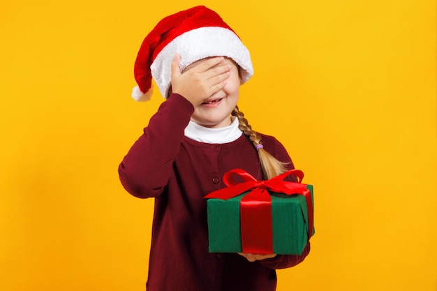 Little girl holds a box with a gift and closed her eyes with her hand.