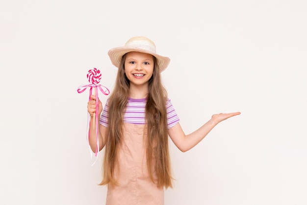 A little girl holds a caramel lollipop in one hand and in the other hand holds your advertisement on a white isolated background