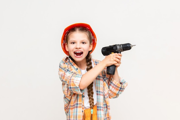 A little girl holds a drill and screams A child in a construction helmet on a white isolated background The concept of renovation in the children's room