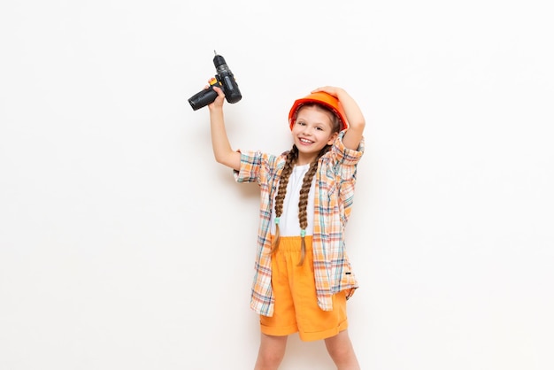 A little girl holds a drill on a white isolated background The child points up at your advertisement The concept of renovation in the children's room