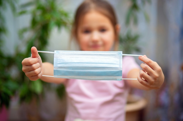 Little girl holds a medical mask in outstretched hands. The child puts on a protective mask