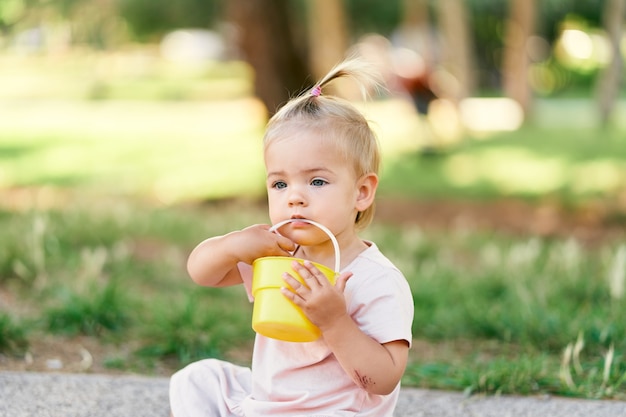 Little girl holds a toy bucket in her hands while sitting on the lawn