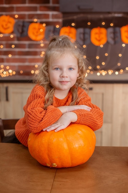 Little girl at home in the kitchen at the table with a pumpkin for halloween