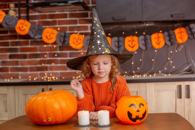 Little girl at home in the kitchen at the table with a pumpkin for halloween