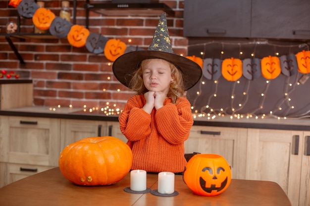 Little girl at home in the kitchen at the table with a pumpkin for halloween